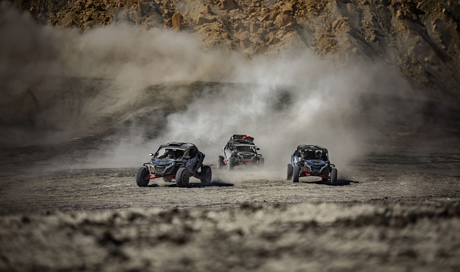 Three Can-Am UTVs driving together through desert dust