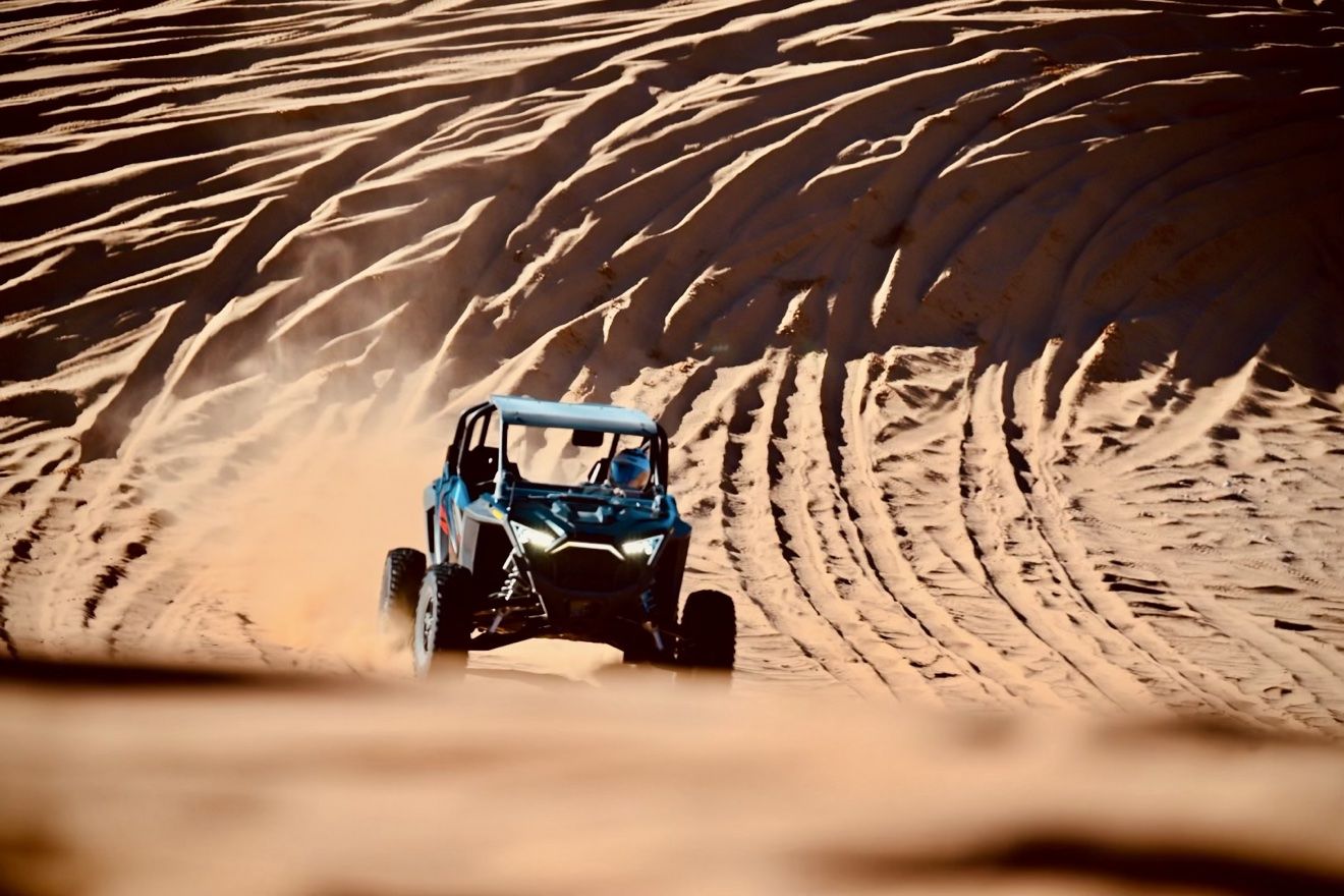 A Can-Am UTV kicking up dust on the Red Sands dunes
